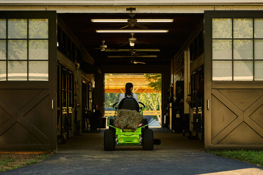 A woman using a Greenworks riding lawn mower in a barn. 
